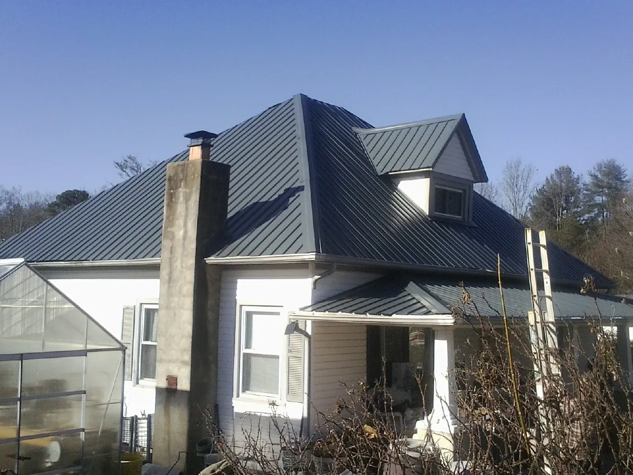 Dark blue standing seam metal roof on a white farmhouse with dormer — Slate & Tile Roof Repair by Roofing Brothers in White Hall