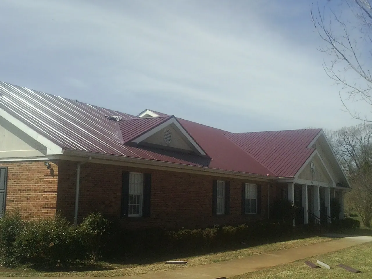 Red metal roof with gabled entries on a long brick building, from a Hail Damage Roof Repair job in White Hall