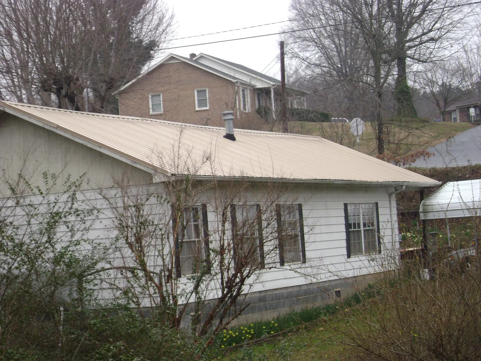Tan metal roof on a white sided house set into a hillside — Commercial Roofing by Roofing Brothers in White Hall