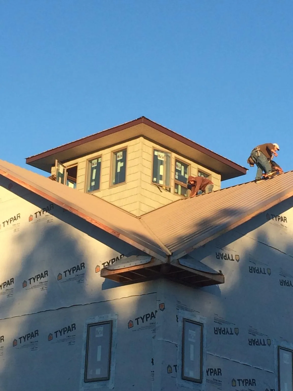 Roofers working around a rooftop cupola on a new metal roof at sunset in White Hall